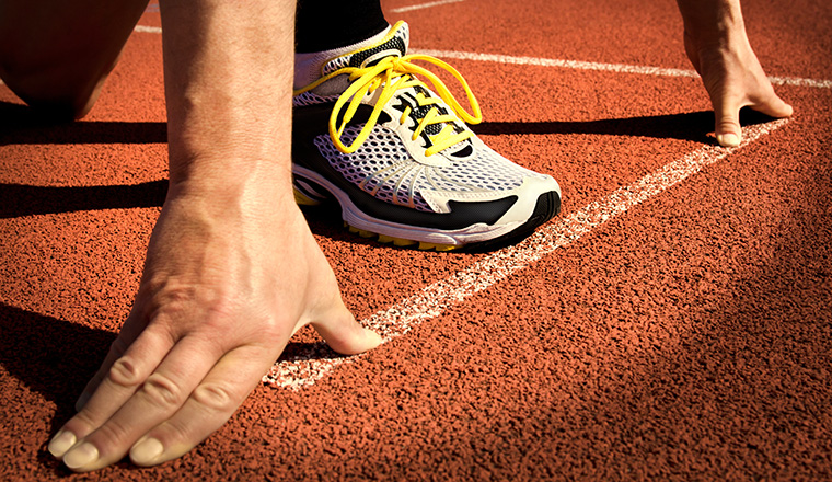 Runner in a stadium is in start position with hands on the line