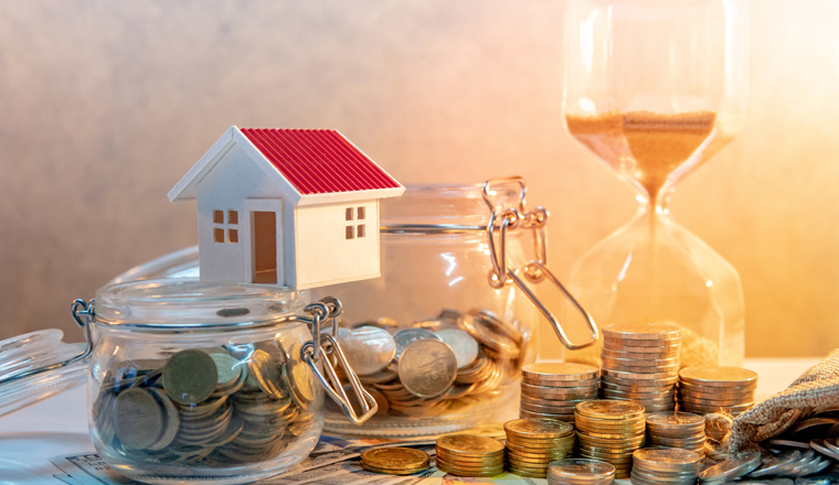 Saving money for retirement concept. Real estate or property investment. Home mortgage loan rate. Coin stack, money bag and currency glass jars on banknotes with hourglasses, house model on the table.