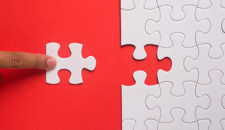 Close up of hand placing the last jigsaw puzzle piece on red background. Business and team work concept.