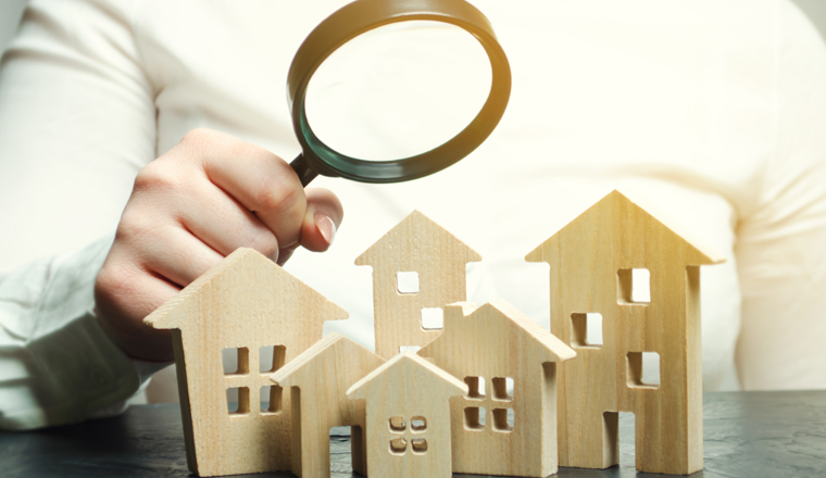 A woman is holding a magnifying glass over a wooden houses. Real estate appraiser. Property valuation / appraisal. Find a house. Search for housing. Real estate market analysis. Selective focus