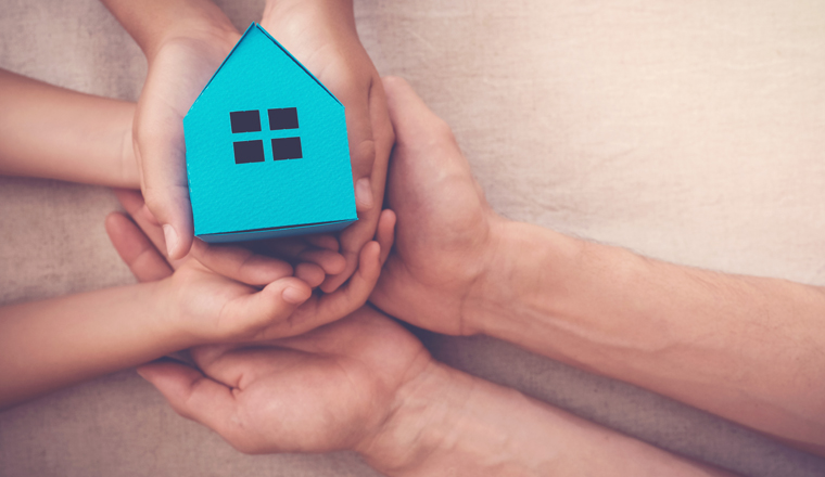 Adult and child hands holding blue paper house for family home and homeless shelter concept