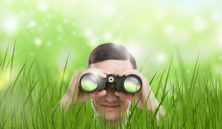 Man looking through binoculars from grass. Lots of copyspace. Head hunting or looking for something concept.