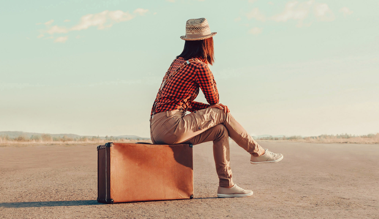 Traveler woman sits on retro suitcase and looks away on road