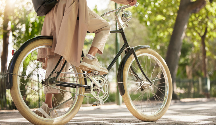 Bicycle, closeup and feet of casual cyclist travel on a bike in a park outdoors in nature for a ride or commuting. Exercise, wellness and lifestyle student cycling as sustainable transport.