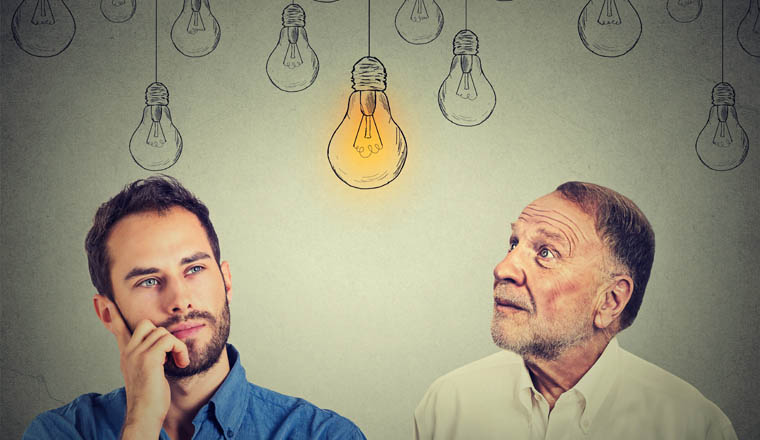 Cognitive skills concept, old man vs young person. Senior man and young guy looking at bright light bulb isolated on gray wall background 