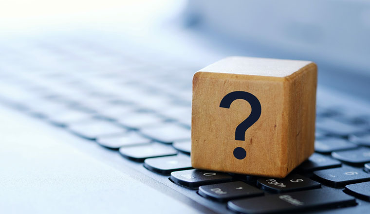 A question mark on a wooden cube on a computer keyboard, with a blurred background and shallow depth of field.