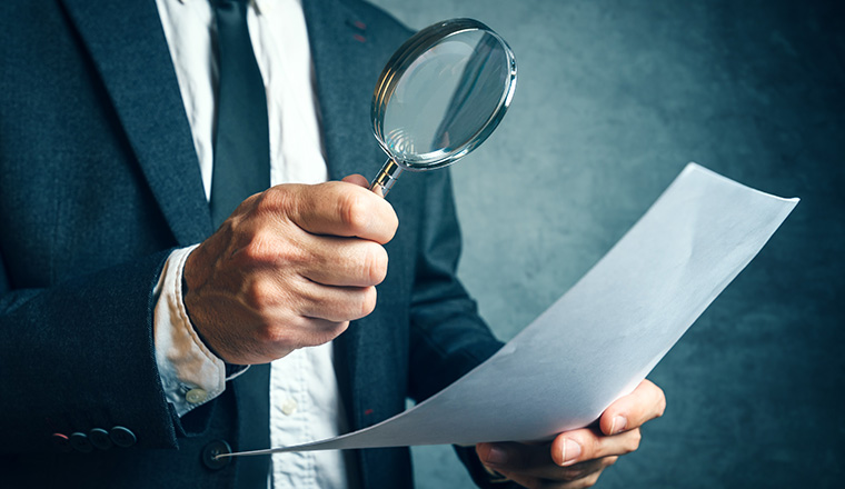 Tax inspector investigating financial documents through magnifying glass, forensic accounting or financial forensics, inspecting offshore company financial papers, documents and reports.