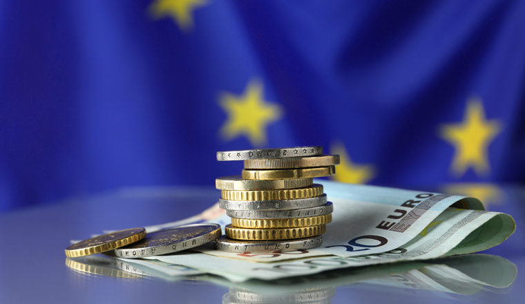 Coins and banknotes on table against European Union flag, space for text