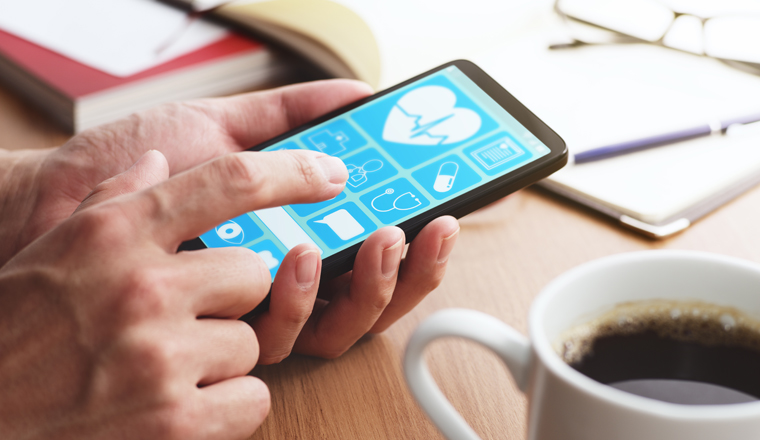 Online healthcare app on smartphone screen. Closeup of male hands touching smartphone screen at table. 