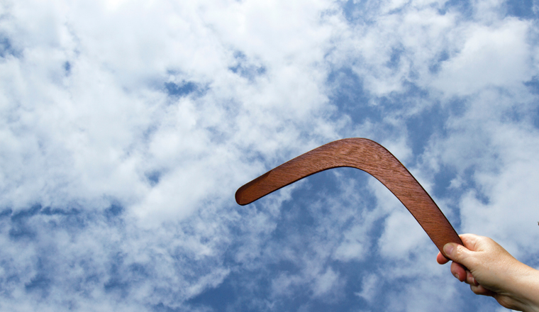 Throwing a wooden boomerang with blue sky and cloud background.