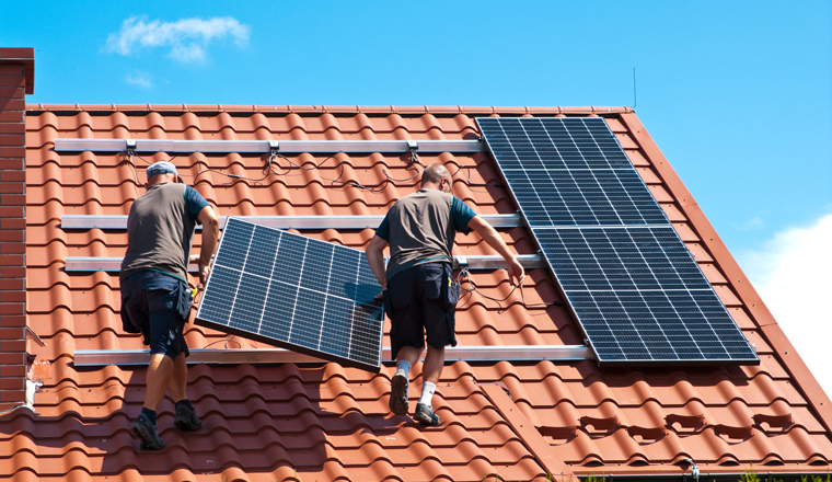 Two men installing new solar panels on the roof of a private house. Renewable energy concept and green energy abstract.