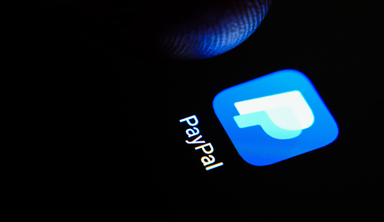 Paypal app icon on the smartphone screen and finger launching it.