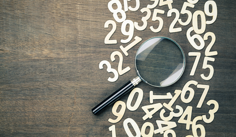 Magnifying glass in scattered numbers on wood background, calculation, mathematics concept
