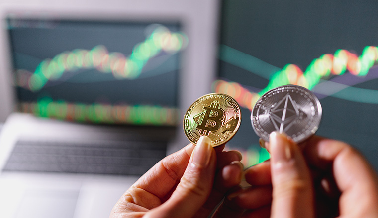 close-up crypto coins. Unrecognizable female hand holds an ethereum and a bitcoin coin with computers representing trend and graphics on background.