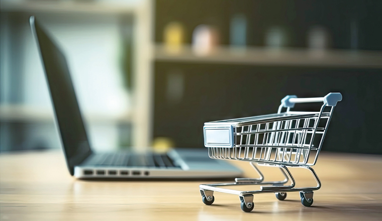 Shopping Cart Model and Laptop on Blurred Home Background. Online Business and E-Commerce Concept