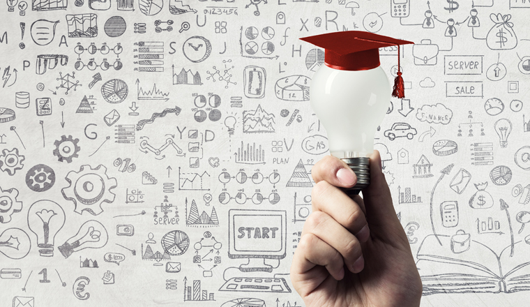 Hand of businessman holding glowing light bulb with graduation hat on it