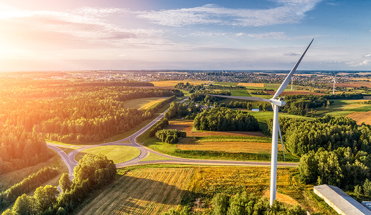 Wind power station. Aerial view. Several wind generators standing at top of the hill. Around are agricultural fields. Frame shows a roundabout and a small city.