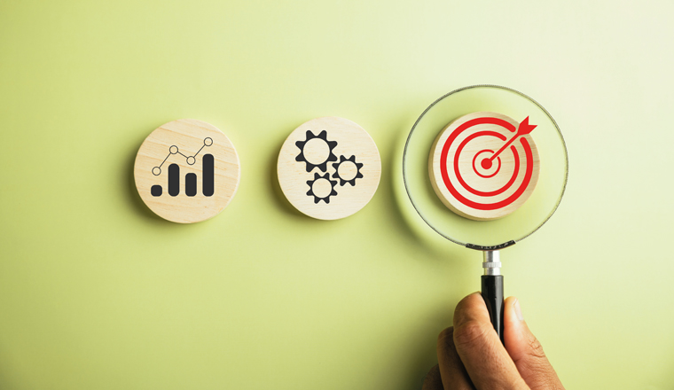 A magnifying glass held by a businessman highlights the target goal icon, signifying the vital role of strategy, sustainable goals, and effective business management for success.