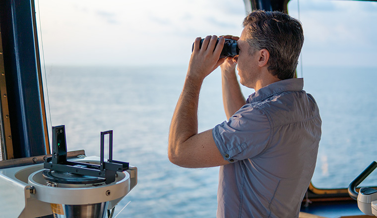 Navigational officer lookout on navigation watch looking through binoculars. Marine industry. COLREG collision regulations