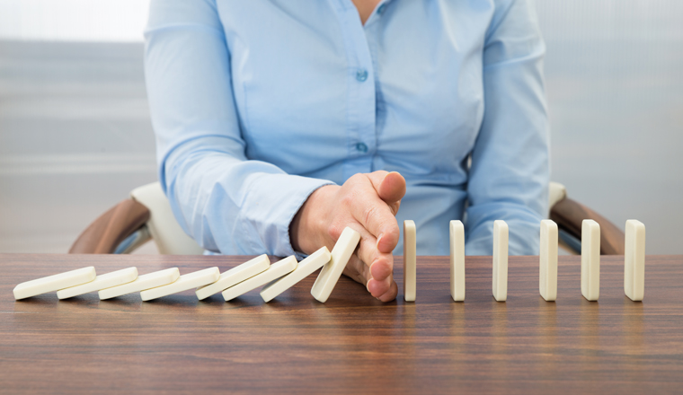 Close-up Of Businesswoman Stopping The Effect Of Domino With Hand At Desk