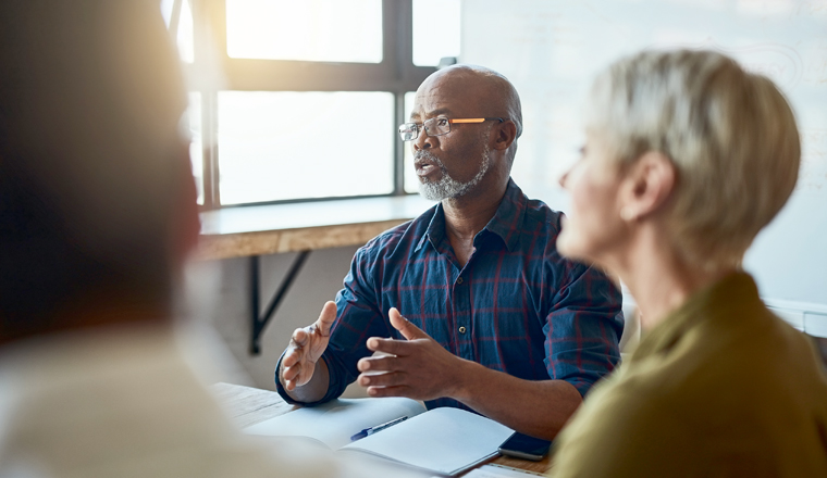 Business people, meeting and leadership of black man in office, talking or speaking. Teamwork, ceo and senior African male professional brainstorming, collaboration or planning strategy in workplace