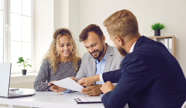 Happy young family at meeting in office signs document on purchase of real estate or loan agreement. Head of bank, realtor or financial advisor submits contract and indicates place of its signing..