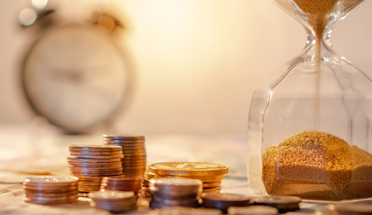 Sand running through the shape of hourglass on table with banknotes and coins of international currency. Time investment and retirement saving. Urgency countdown timer for business deadline concept