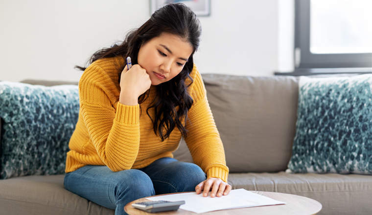 accounting, taxes and finances concept - sad young asian woman with papers and calculator at home