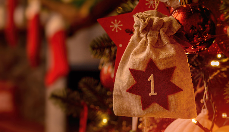 Christmas background. Advent calendar. Advent calendar in the form of an eco bag hangs on the Christmas tree against the background of the Christmas room with a fireplace and Santa's boots.