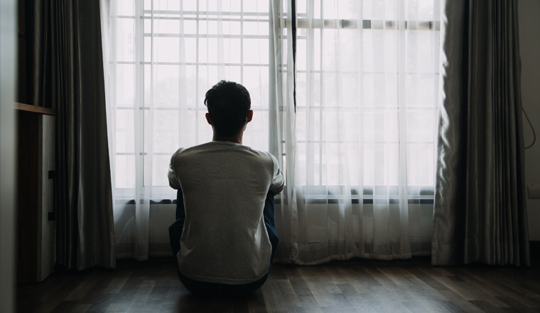 Alone man silhouette staring at the window closed with curtains in bedroom. Man stands at window alone