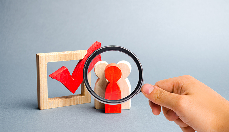 Magnifying glass is looking at the people stand near the checkbox for voting in elections. Lobbying interests, election corruption, voter bribery, and rigging election results. Selective focus