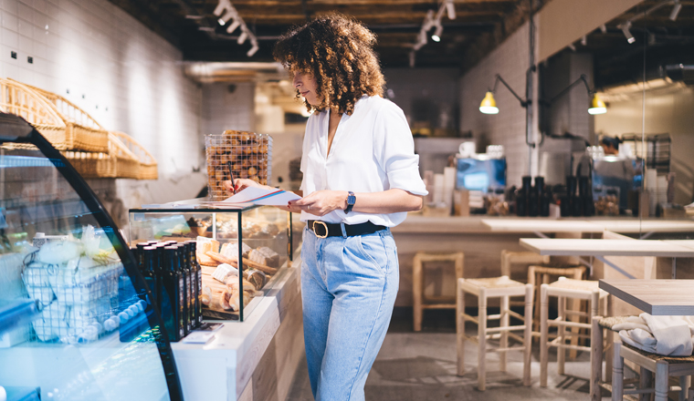 Smart casual female manager checking showcase goods and analyzing paper statistics in own cafeteria, self employed Caucaisan woman working with report improve skills in franchise experience