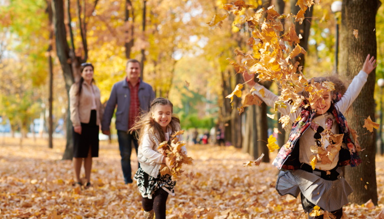 Happy family is in autumn city park. Children and parents running with leaves.. They posing, smiling, playing and having fun. Bright yellow trees.