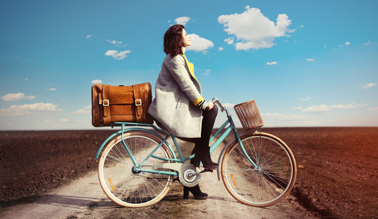 portrait of a young woman with a bicycle and suitcase standing in the middle of the field