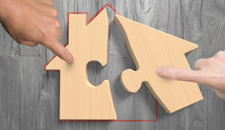 Man and woman two hands assembling wooden house shape puzzles, high angle view, on wood plank background.