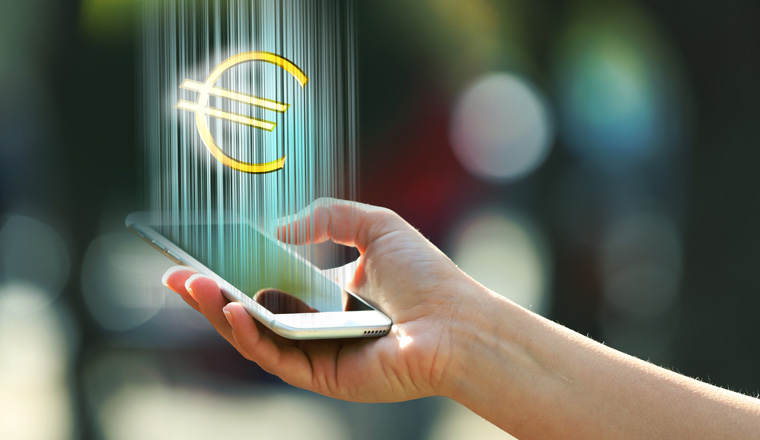 Hand holding a mobile phone with euro sign outdoors, on blurred background