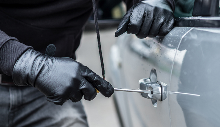 Car thief trying to break into a car with a screwdriver. Car thief, car theft.