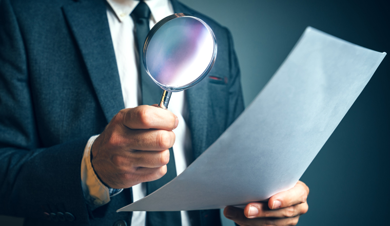 Lawyer reading legal contract agreement disclaimer with magnifying glass, person in elegant business suit reading document.