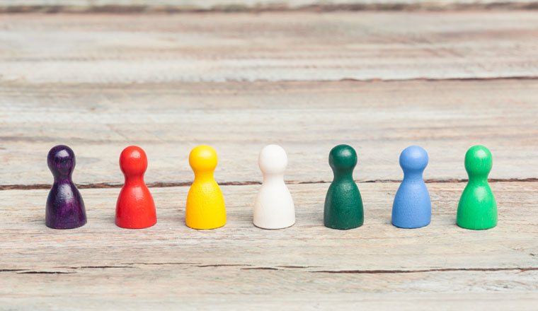 sieben unterschiedlich gefärbte Spielfiguren in einer Gruppe auf einem Holztisch