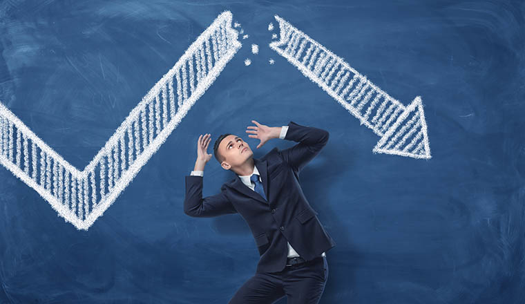 Businessman cowering on blue blackboard background with chalk drawing of white statistic arrow broken in half. Business management. Profit and loss. Business and success.