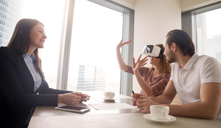 Young woman wearing virtual reality glasses or goggles, couple using head-mounted display for real estate tours, excited by participation effect, virtually discover new flat, buy and sell homes in VR