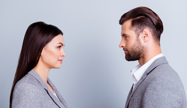 Concept of confrontation in business. Close up photo of two young serious confident people standing face-to-face to each other