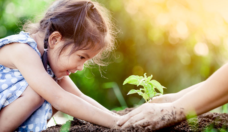 Asian little girl and parent planting young tree on black soil together as save world concept in vintage color tone