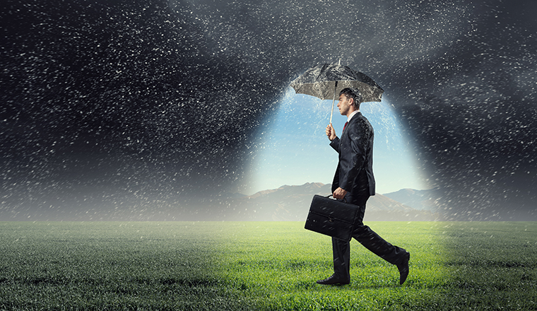 Young businessman with umbrella under rain walking on field