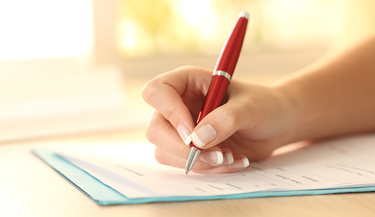 Close up of a woman hand using a pen to filling form on a table