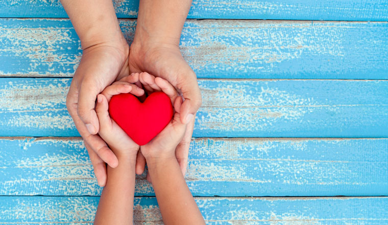 Red heart in child kid and mother hands on old blue wooden table in vintage retro style