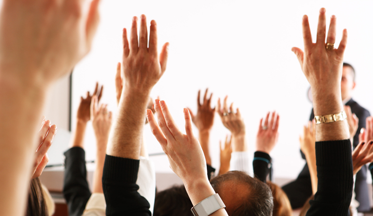 Raised hands and arms of large group of people in class room, audience voting in professional education surrounding, selective focus with anonymous people.