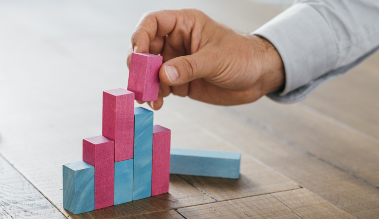 Businessman working at office desk, he is building a growing financial graph using wooden toy blocks: successful business concept