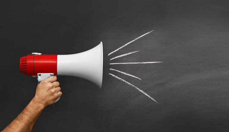 Hand holding megaphone over chalkboard background with copy space