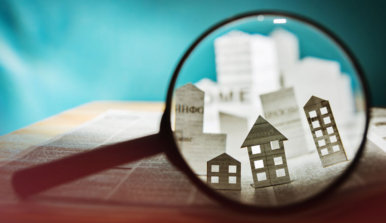 Magnifying glass in front of an open newspaper with paper houses. Concept of rent, search, purchase real estate.